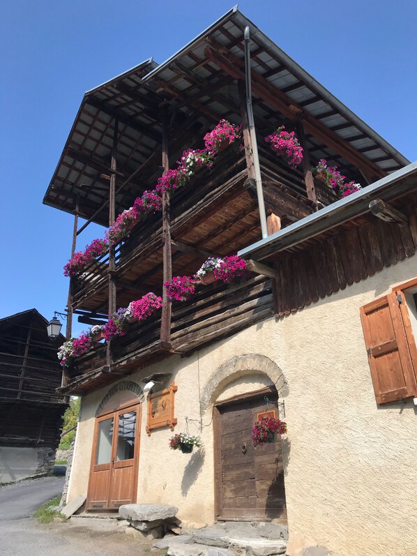 Ein traditionelles Chalet mit hölzernen Balkonen, die mit Blumen geschmückt sind, Steinstufen und einer rustikalen Fassade.