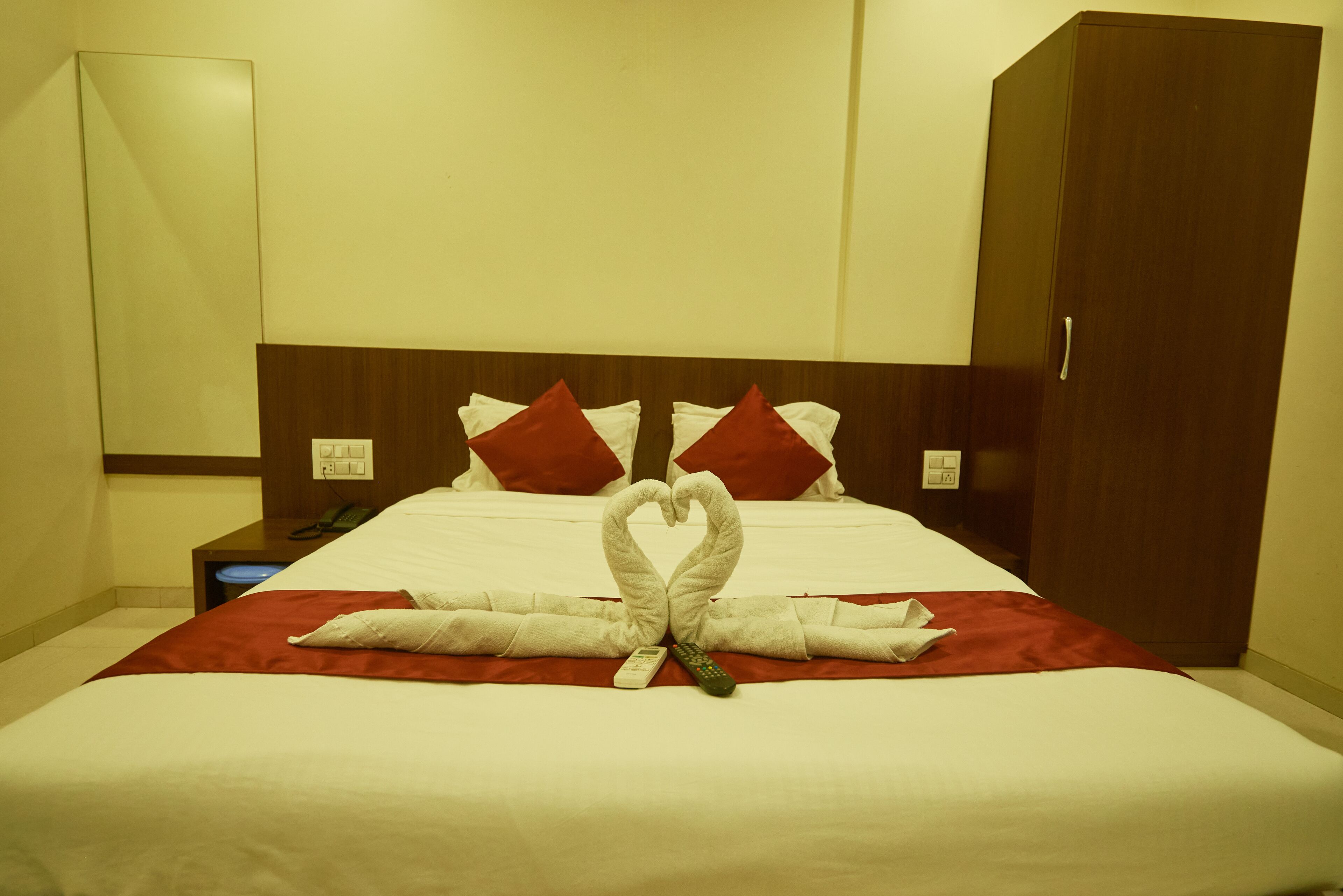 A hotel room with a neatly made bed, a wooden headboard, and a wardrobe.