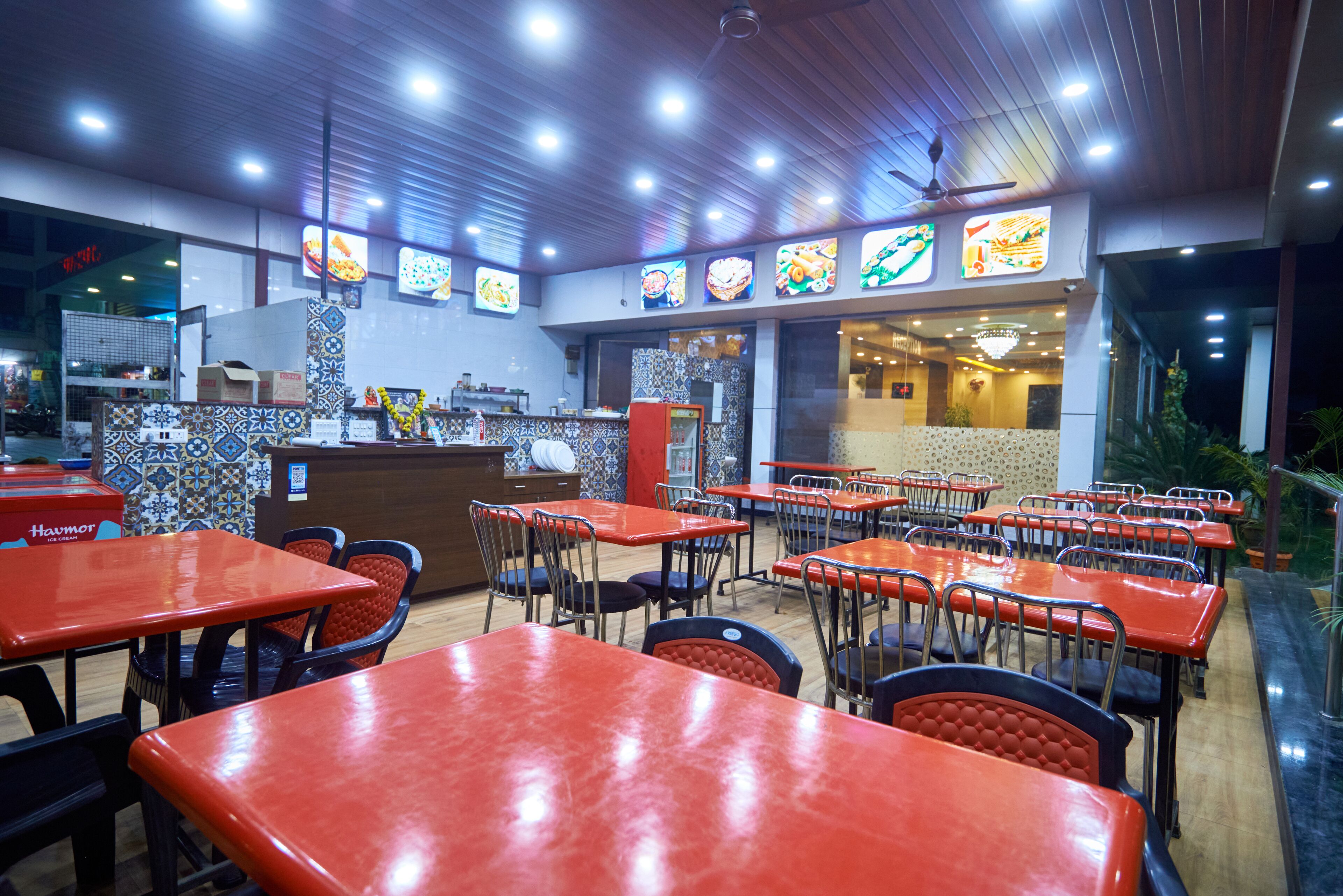 A restaurant interior with multiple tables and chairs, a counter with a menu display, and a ceiling fan.