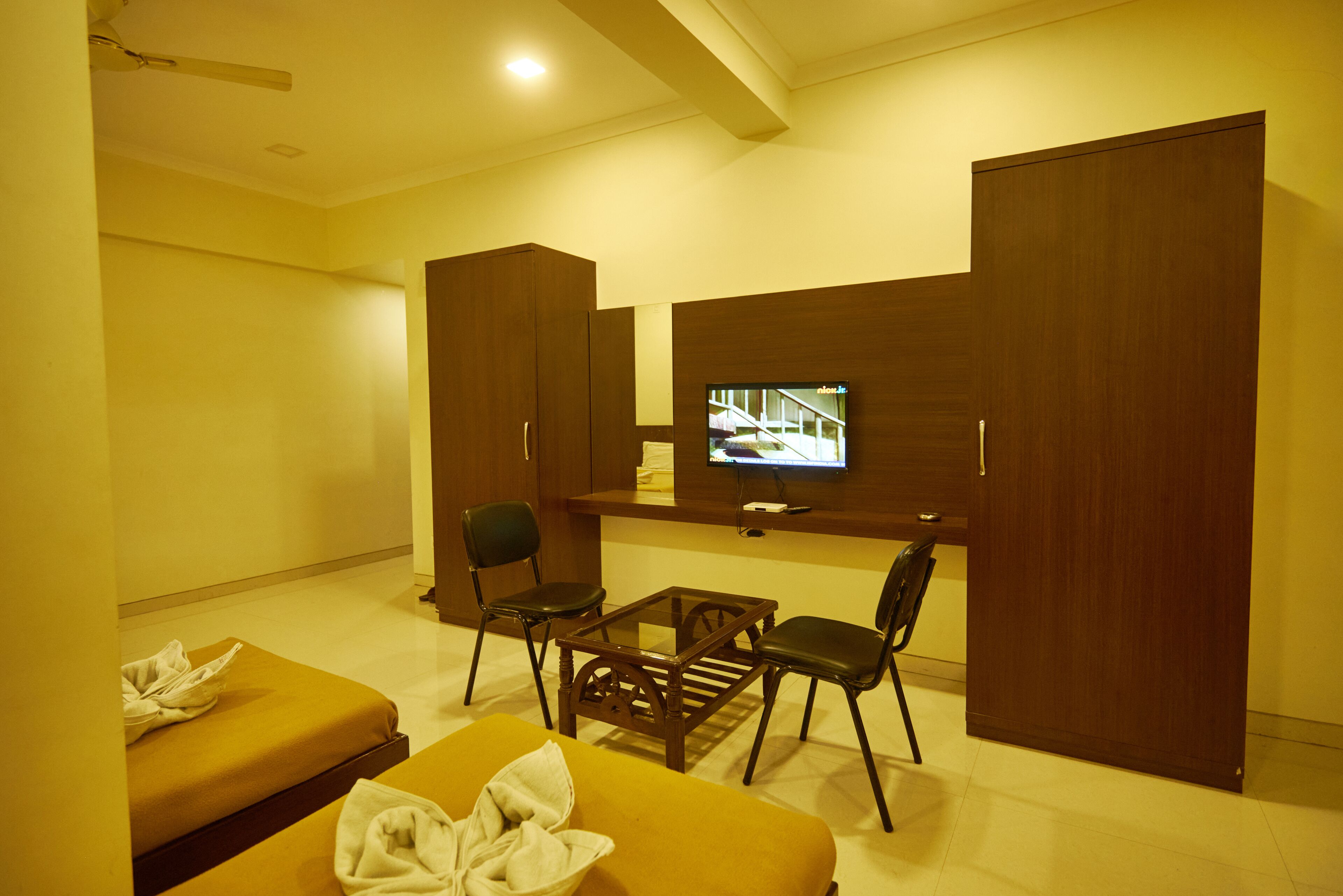 A hotel room with a TV, two sofas, a coffee table, and wooden wardrobes.