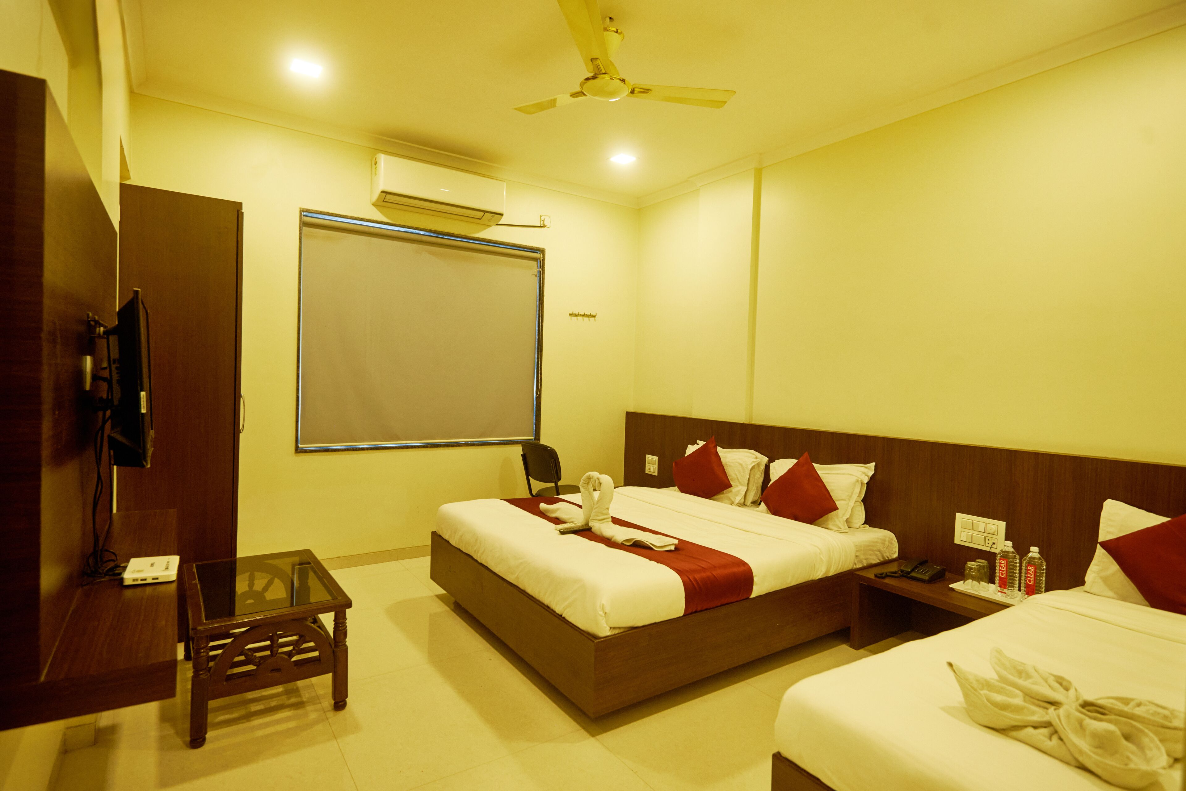 A hotel room with two beds, a small table, a nightstand, and a ceiling fan.