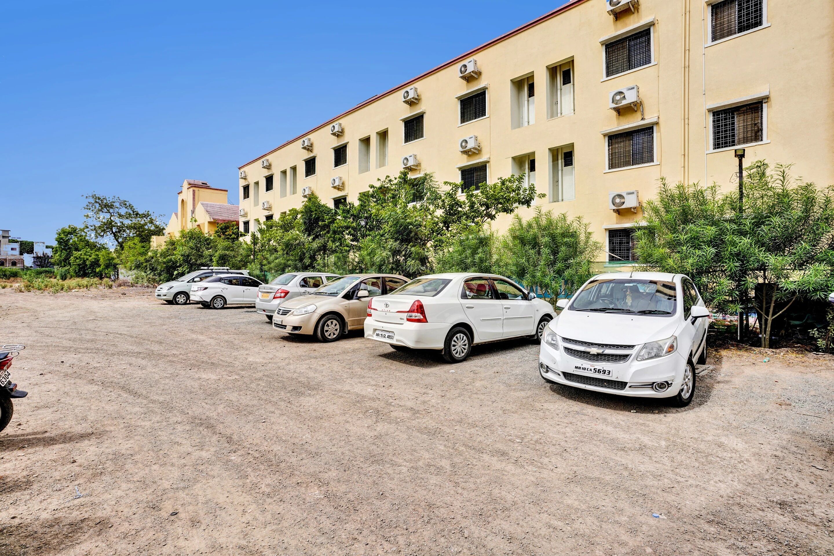 A parking lot with several cars parked in front of a building with multiple air conditioning units.