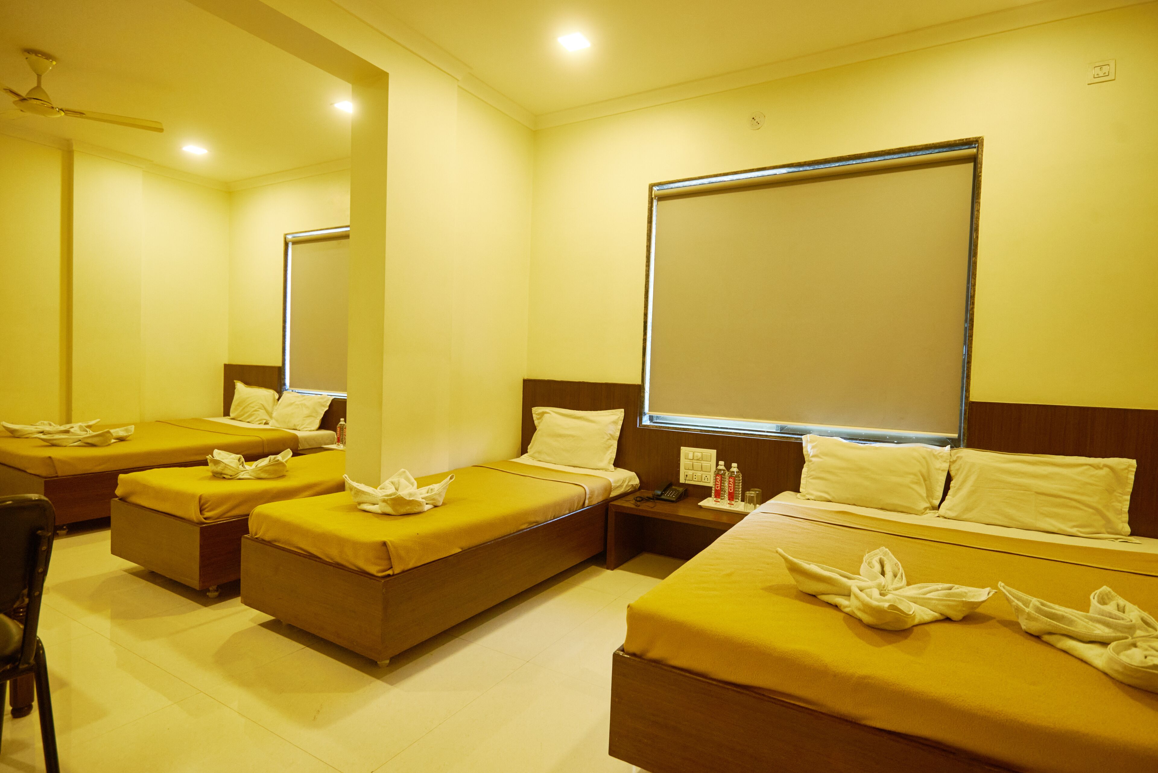 A hotel room with four single beds, a desk, a chair, and a large window.