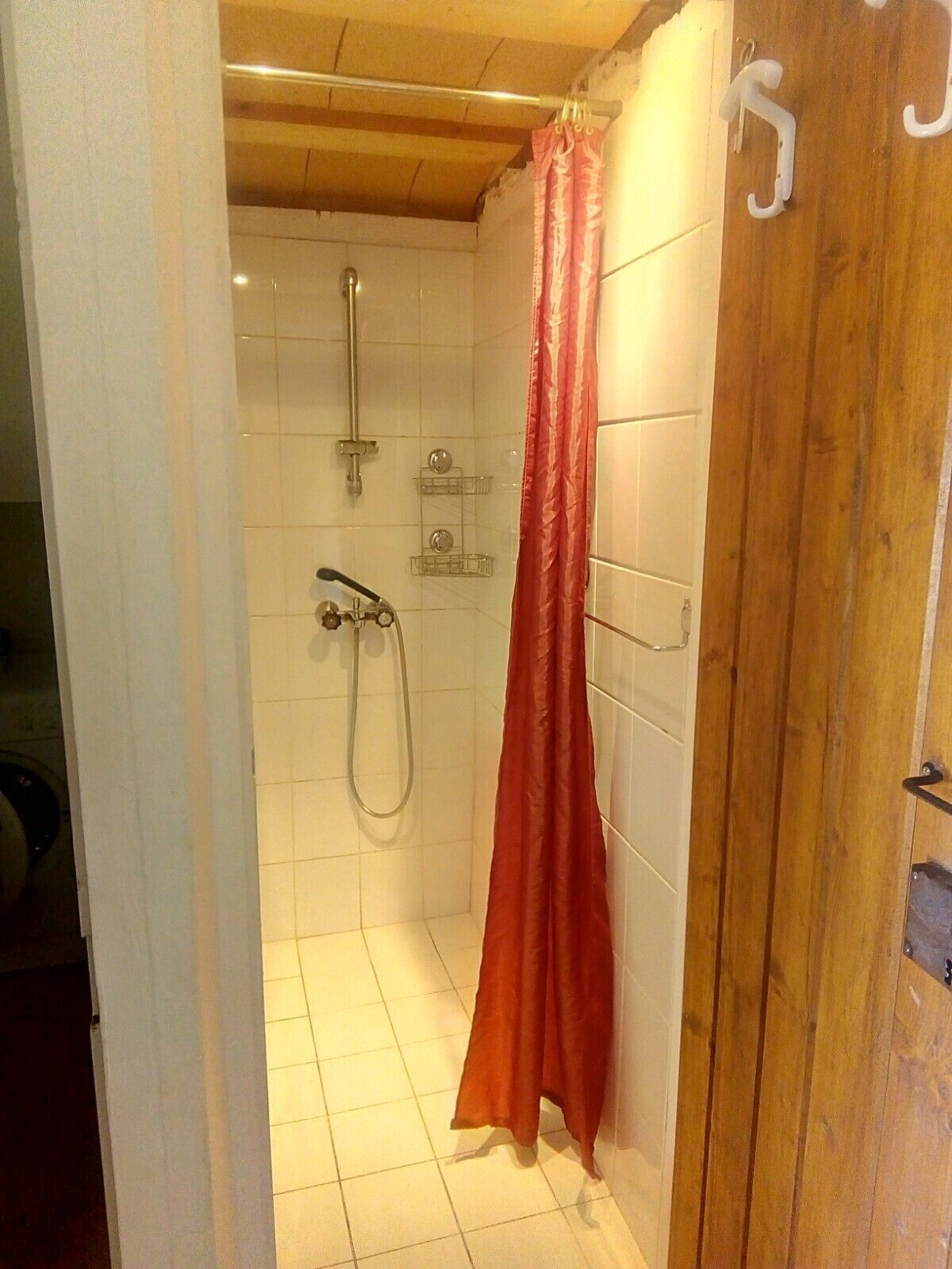 Un petit espace douche fermé, équipé d’un pommeau de douche, d’un pommeau de douche à main et d’un rideau de douche rouge.