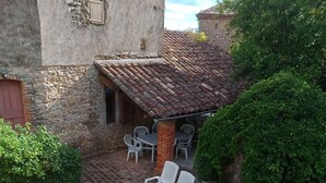 A rustic stone building with a tiled roof, a gravel patio, and two white lounge chairs.