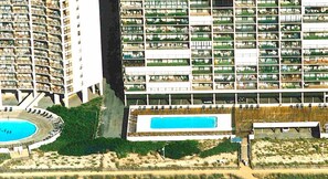 Een hoog hotel met meerdere balkons, een zwembad en een aangelegde tuin.