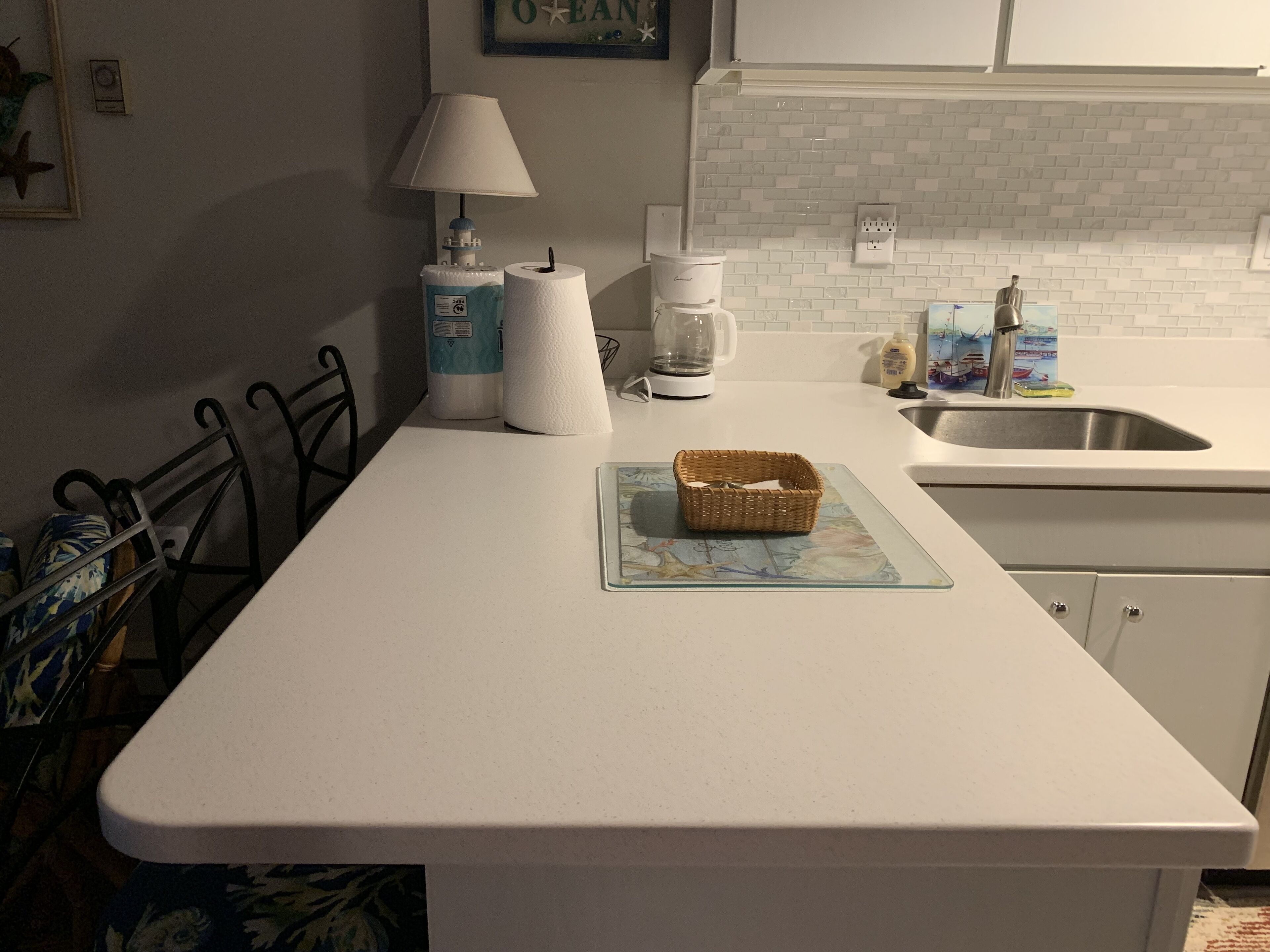 Een keuken met een wit aanrecht, een koffiezetapparaat, een mand en een spoelbak.