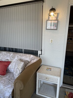 Een gezellige kamer met een bed, een klein wit rieten tafeltje, een wandlamp en een bord met de route voor evacuatie bij nood.