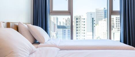 Habitación de hotel con cama, ventana con cortinas y vista a la ciudad.