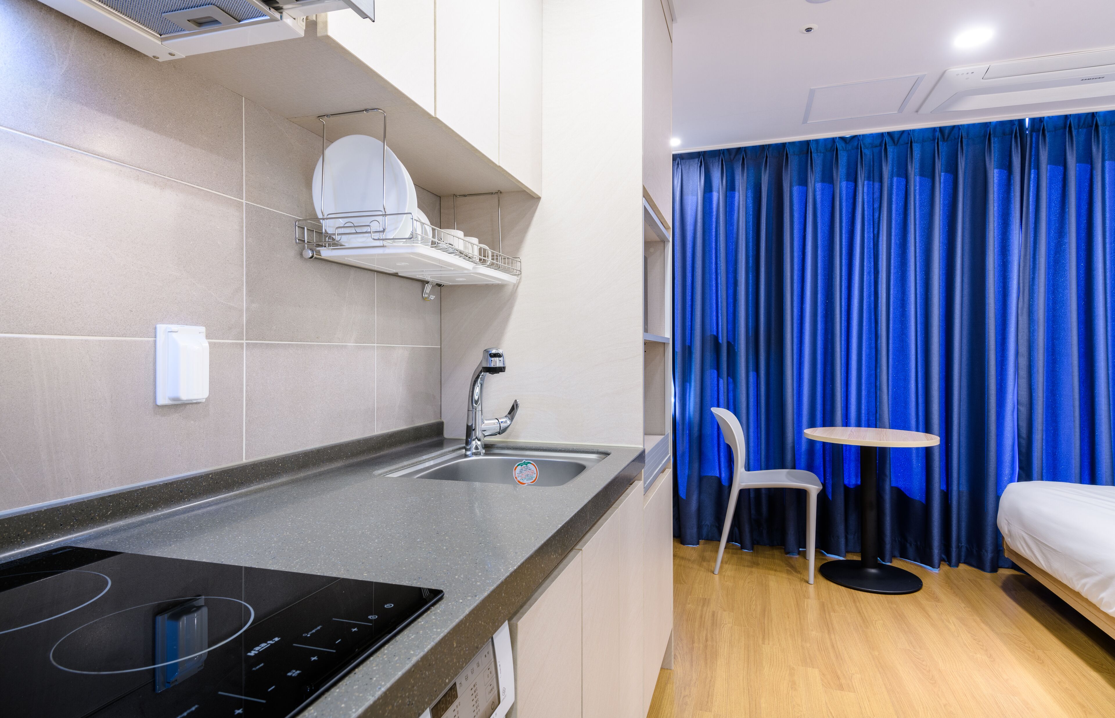 A compact hotel room with a kitchenette, a single bed, a small table, and a chair.
