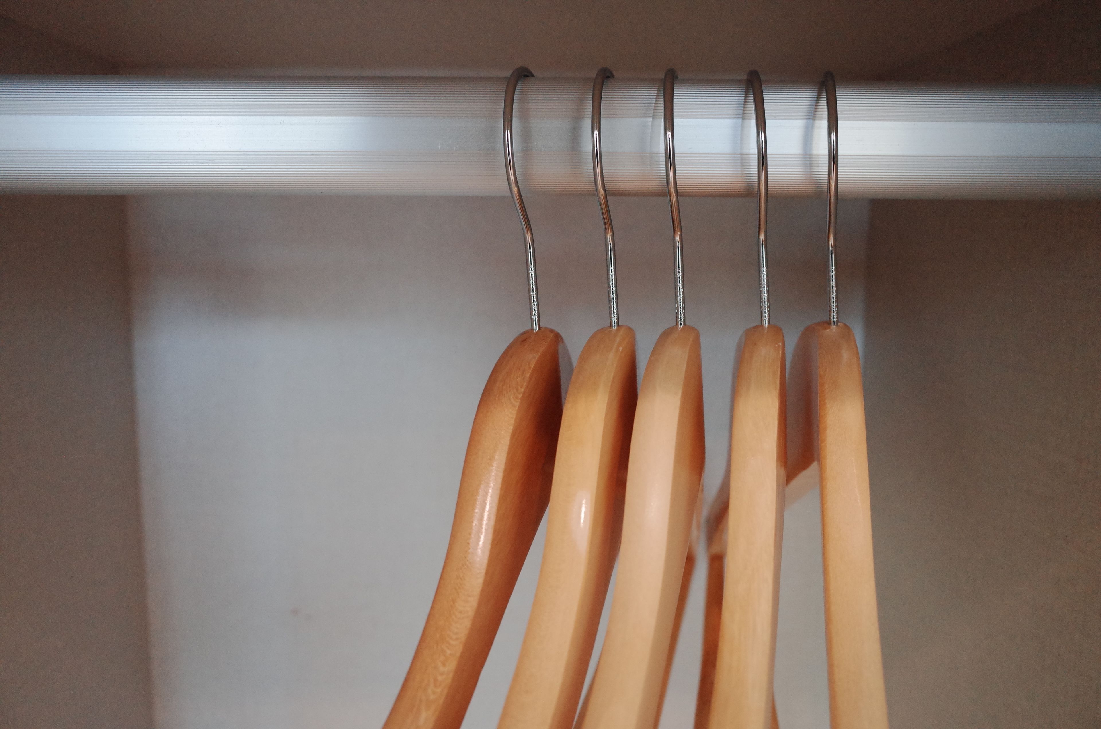 A closet with wooden hangers on a rod.