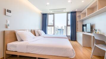 Ein modernes Hotelzimmer mit zwei Betten, einem Schreibtisch und einem großen Fenster mit Blick auf die Stadt.