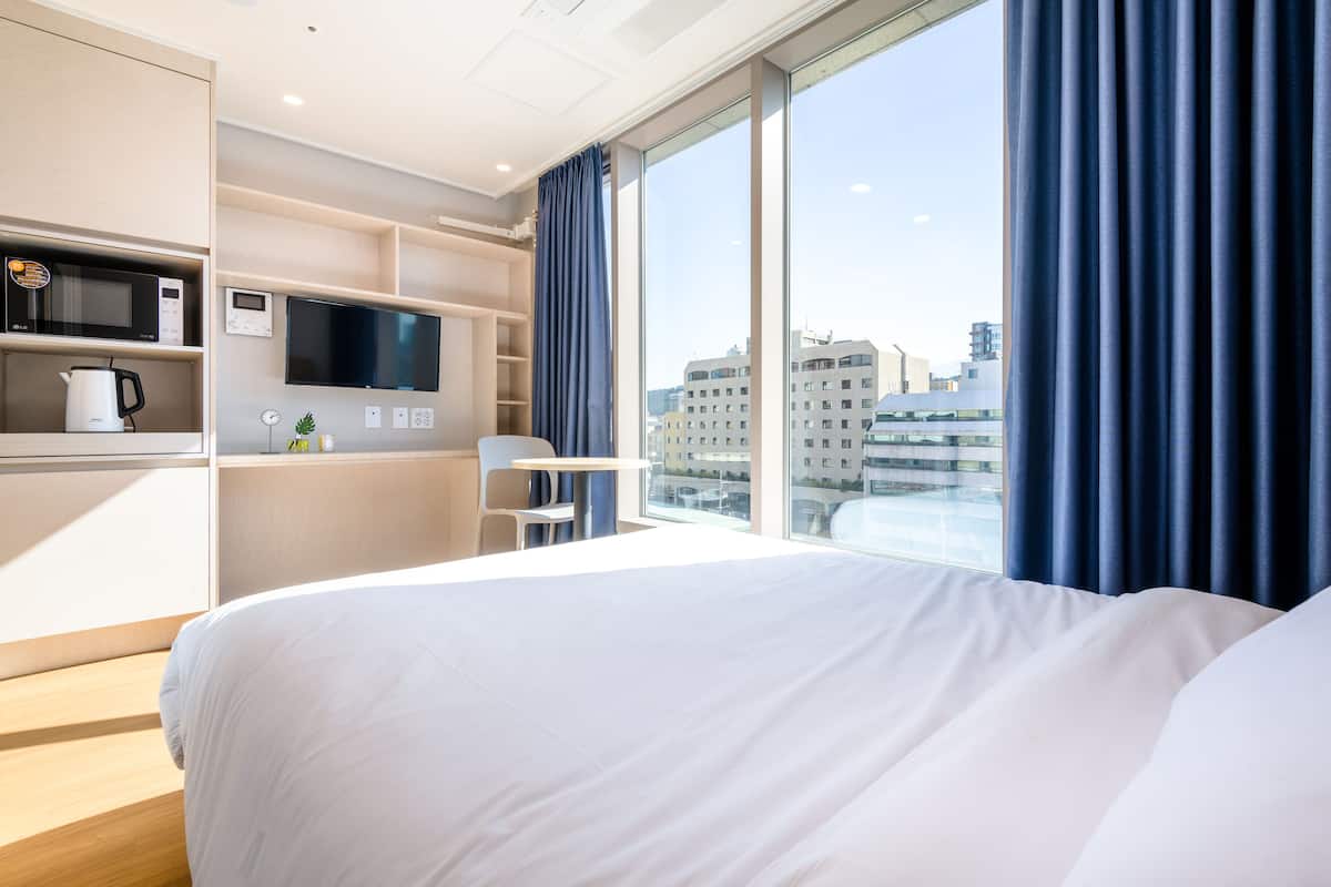 A hotel room with a bed, a TV, a microwave, and a coffee maker on a shelf.