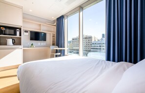 A hotel room with a bed, a TV, a microwave, and a coffee maker on a shelf.
