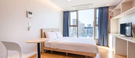 A modern hotel room with a bed, a desk, a chair, and a large window offering a city view.