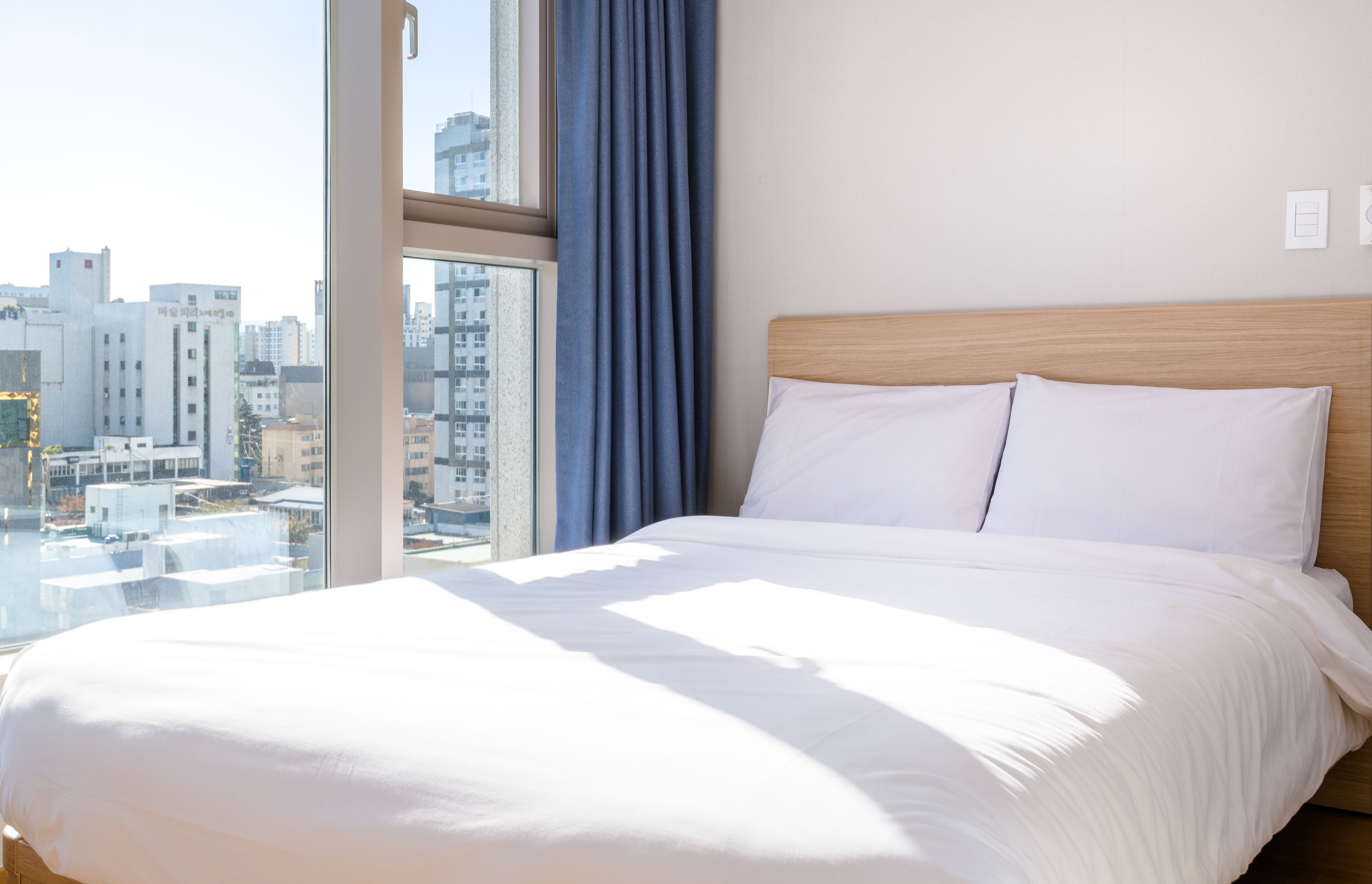 A hotel room with a large bed, a view of the city through a window, and a curtain.