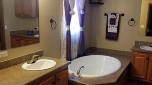 A bathroom with two sinks, a large bathtub, wooden cabinets, a mirror with lights, and a towel rack. - American Pines Lodge, 5 miles from Mt. Rushmore (Keystone)
