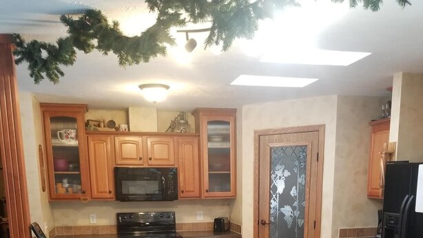 A kitchen with wooden cabinets, a microwave, a stove, and a refrigerator. There are three bar stools in front of the counter. - American Pines Lodge, 5 miles from Mt. Rushmore (Keystone)