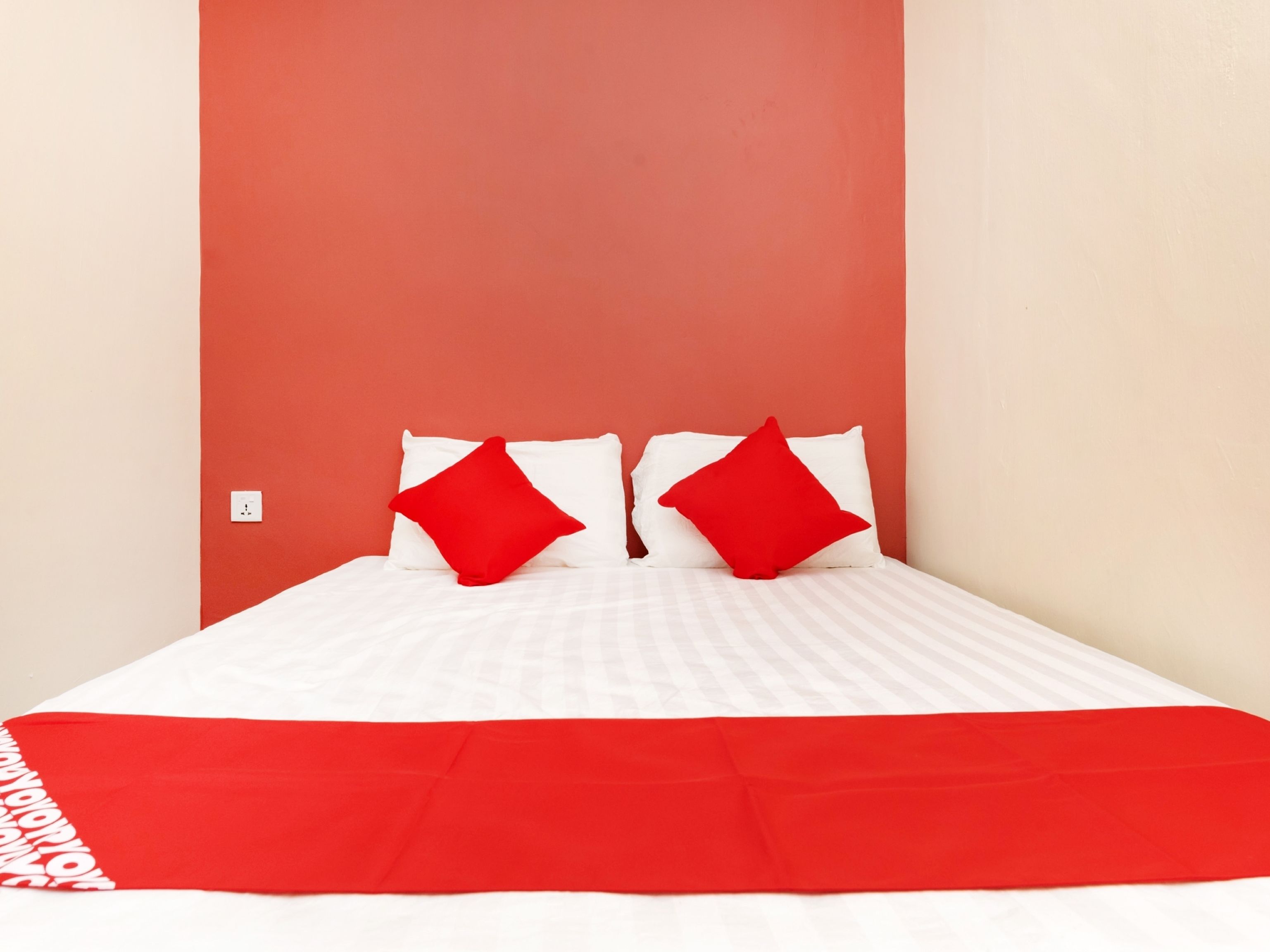 Un lit avec une literie blanche et des touches de rouge, notamment des coussins et une couverture.