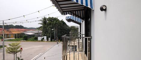 Un balcón con un toldo a rayas, baranda de metal y vista a una calle con edificios y árboles.