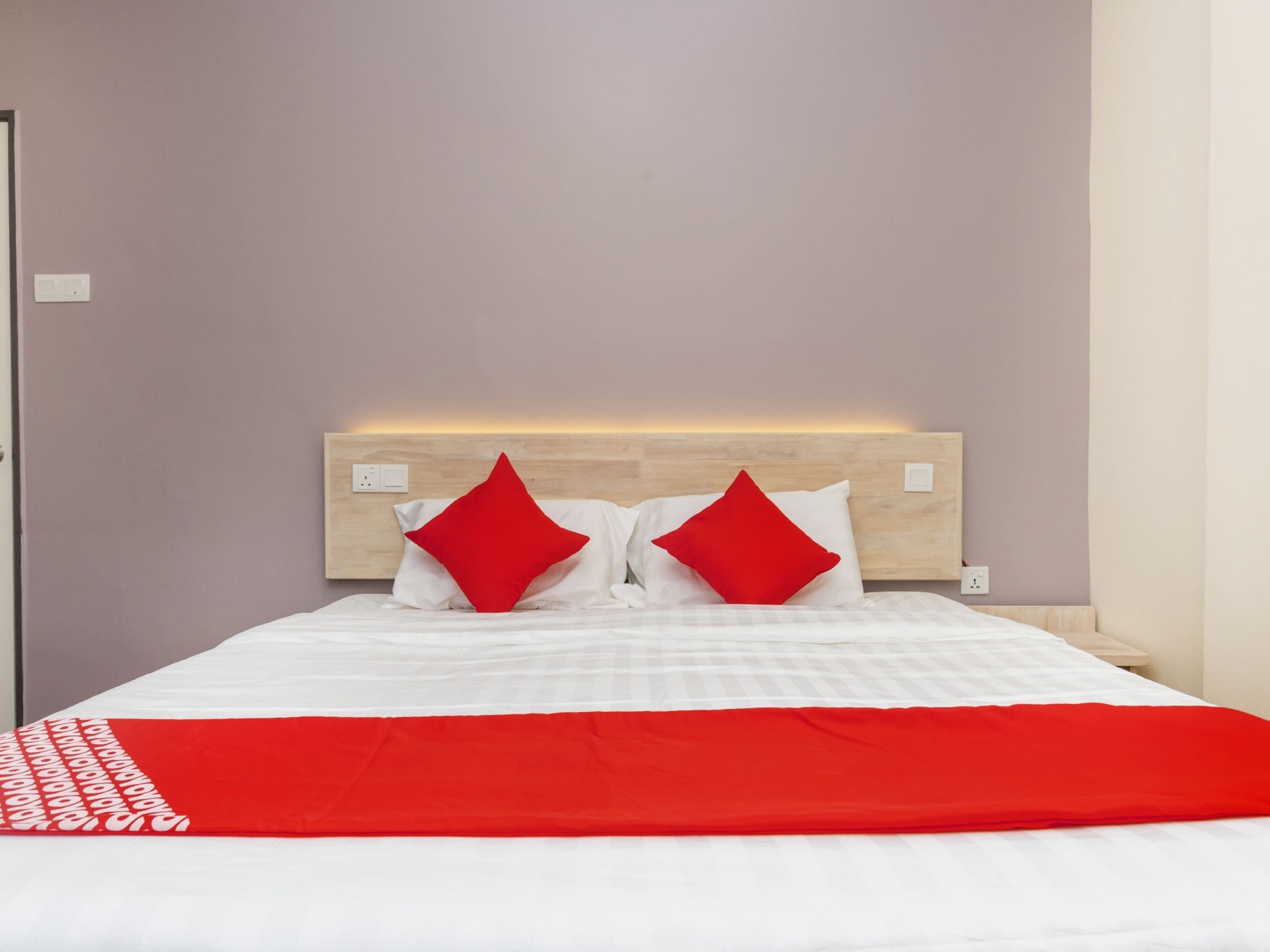 A neatly made bed with a red and white bedspread and two red pillows.