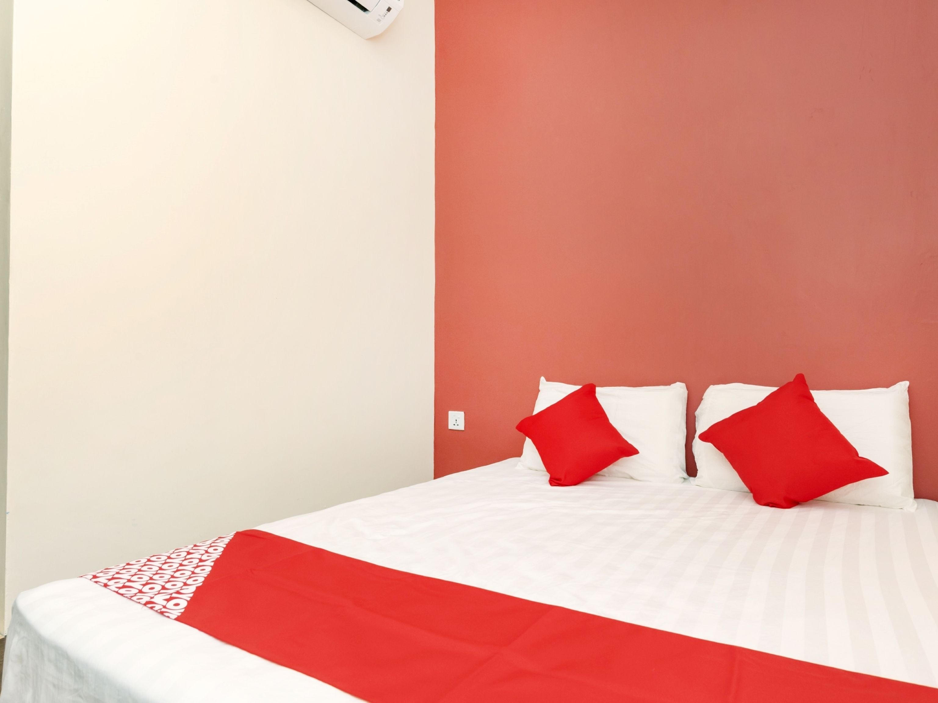 A hotel room with a bed, two red pillows, and a red and white bedspread.