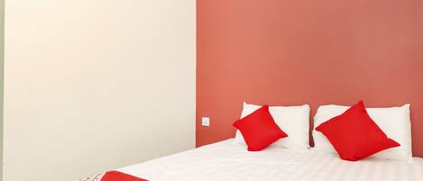 A hotel room with a bed, two red pillows, and a red and white bedspread.
