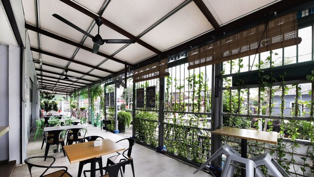 An indoor cafe with tables and chairs, large windows with plants, and a ceiling fan. - OYO 778 BMW 2 Hotel (Muar)