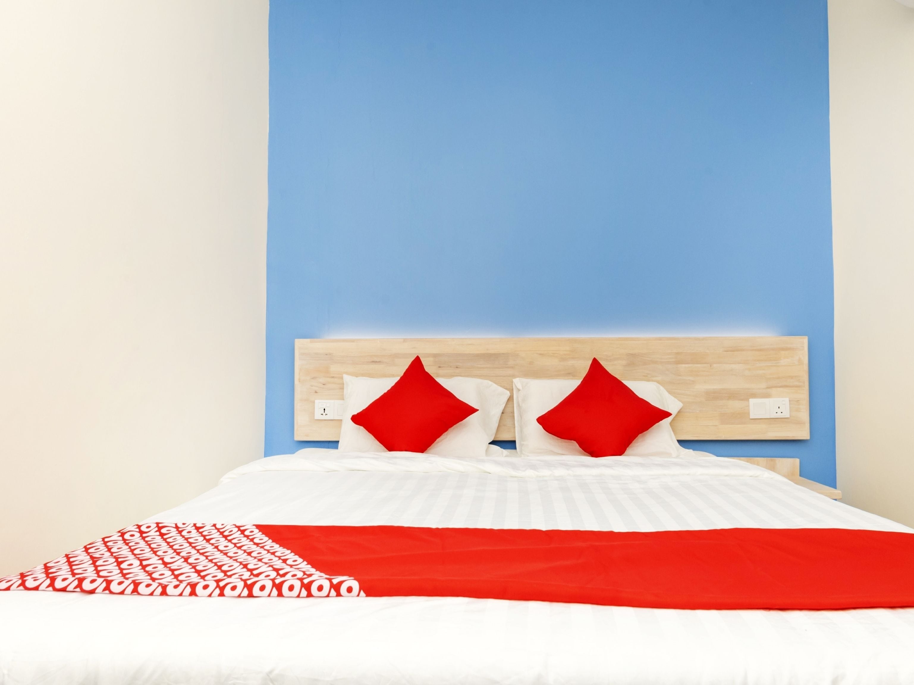 A bed with a wooden headboard, white bedding, and red accents.