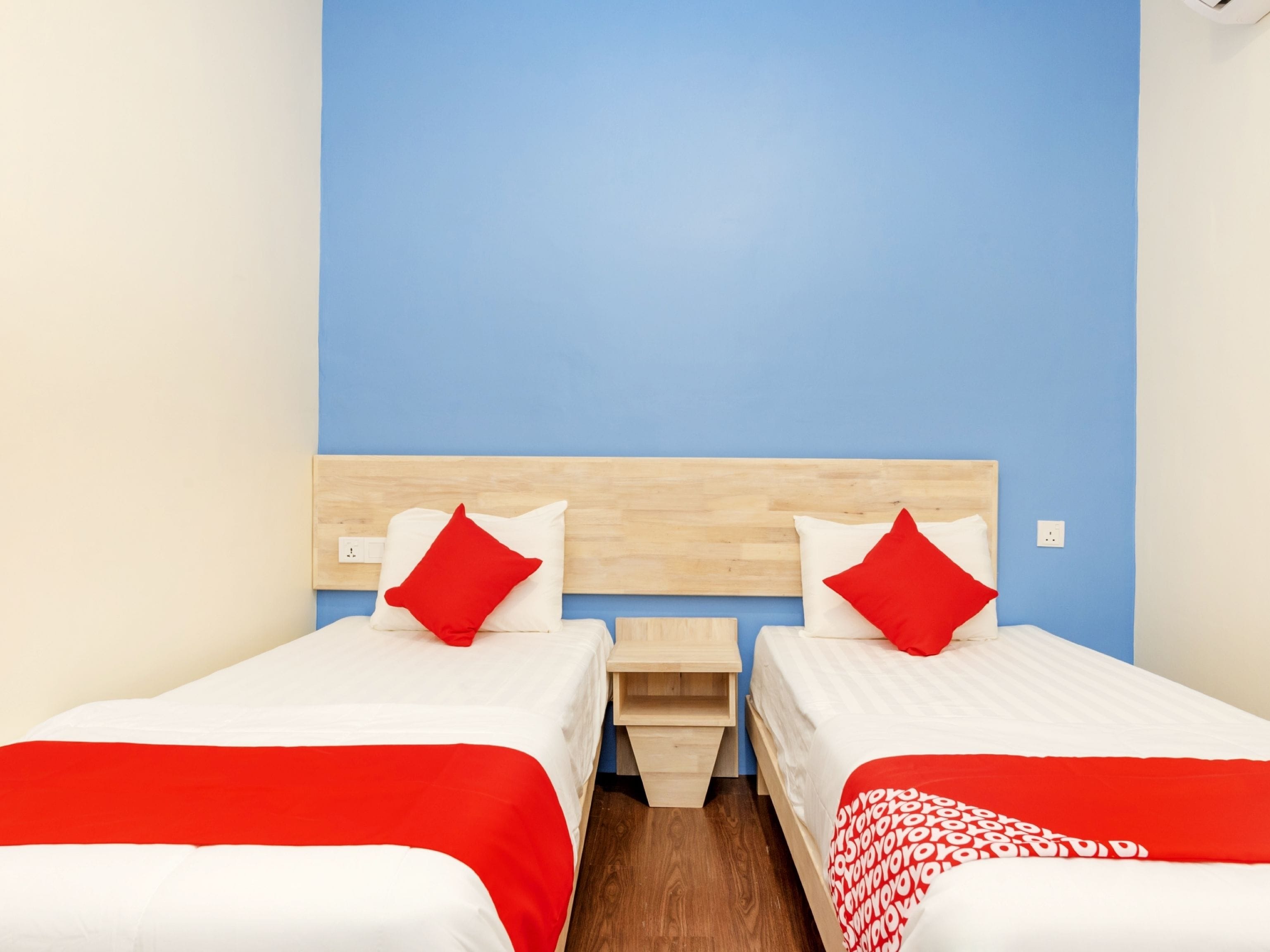 A hotel room with two single beds, each with a red and white bedspread and pillows, a wooden headboard, and a blue accent wall.