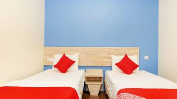 A hotel room with two single beds, each with a red and white bedspread and pillows, a wooden headboard, and a blue accent wall.