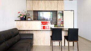 A modern living room with a sofa, two chairs, a TV, and a kitchen area with wooden cabinets and a refrigerator. - OYO 778 BMW 2 Hotel (Muar)