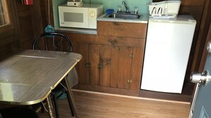 A compact kitchen with a wooden table, chairs, a microwave, a sink, and a refrigerator.
