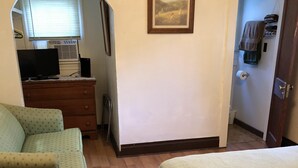 A room with a bed, a chair, a dresser, a television, and a framed picture on the wall.