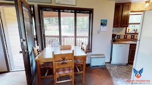A kitchen with wooden cabinets, a dining table with chairs, a small refrigerator, and a window with a view of trees.