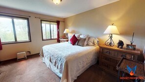 A bedroom with a large bed, two bedside lamps, a wooden dresser, and a window with curtains.