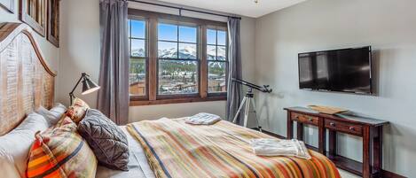 Une chambre d’hôtel équipée d’un lit, d’un bureau, d’une télévision et d’une fenêtre donnant sur la montagne.