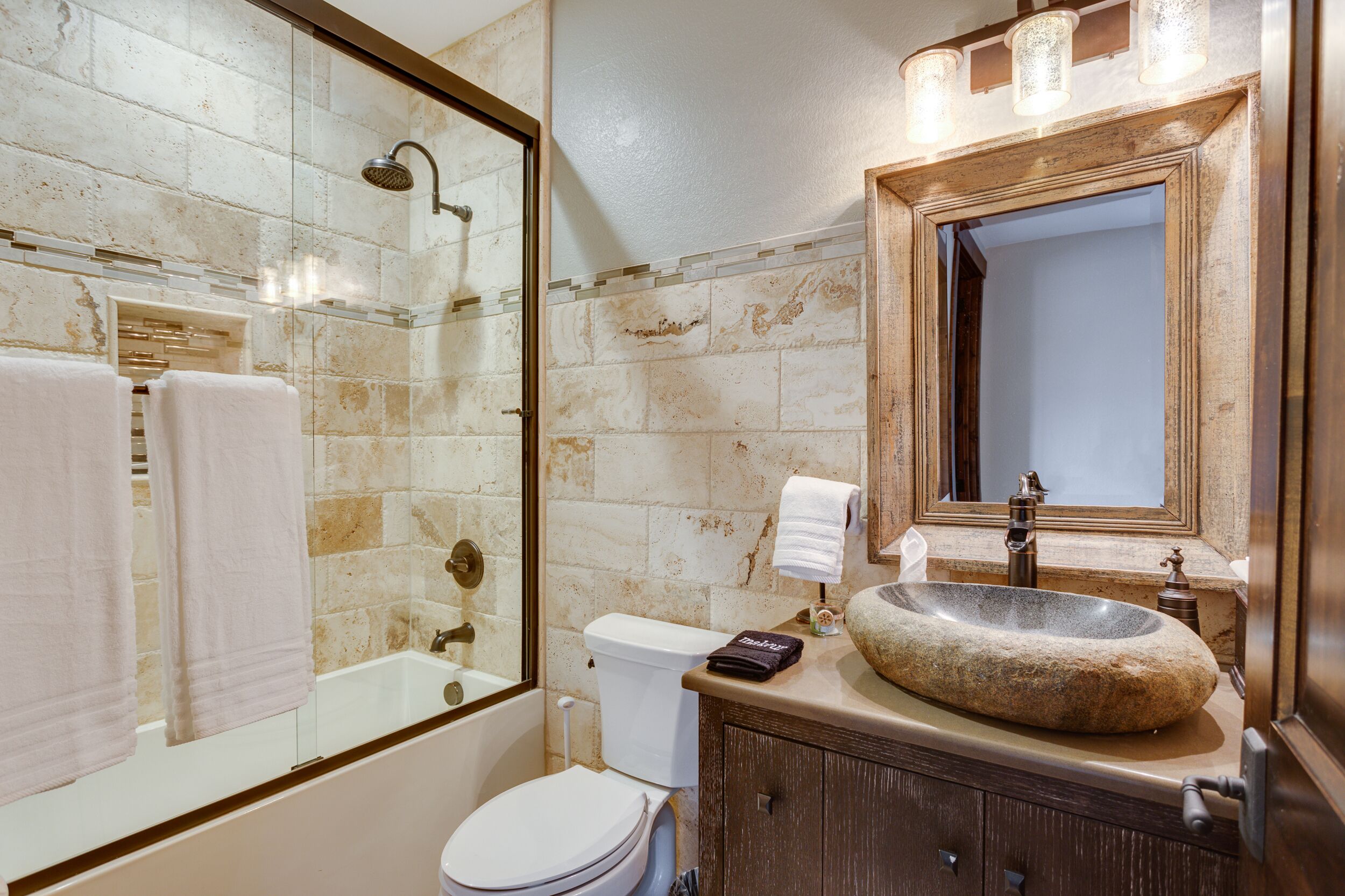 A bathroom with a stone sink, a glass-enclosed shower, and a wooden vanity.