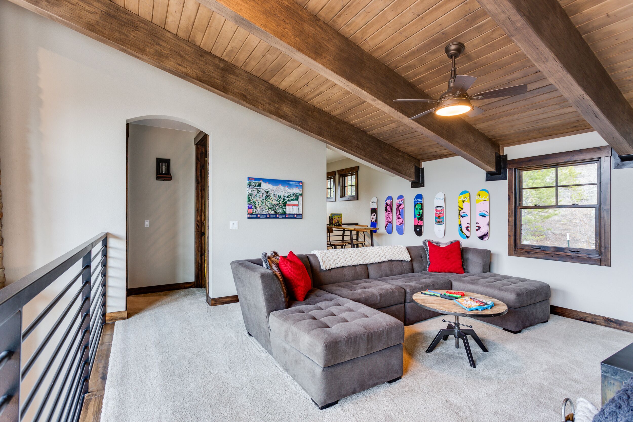 A spacious living room with a large gray sectional sofa, a wooden ceiling, and a small table with a laptop.