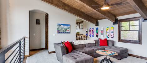A spacious living room with a large gray sectional sofa, a wooden ceiling, and a small table with a laptop.
