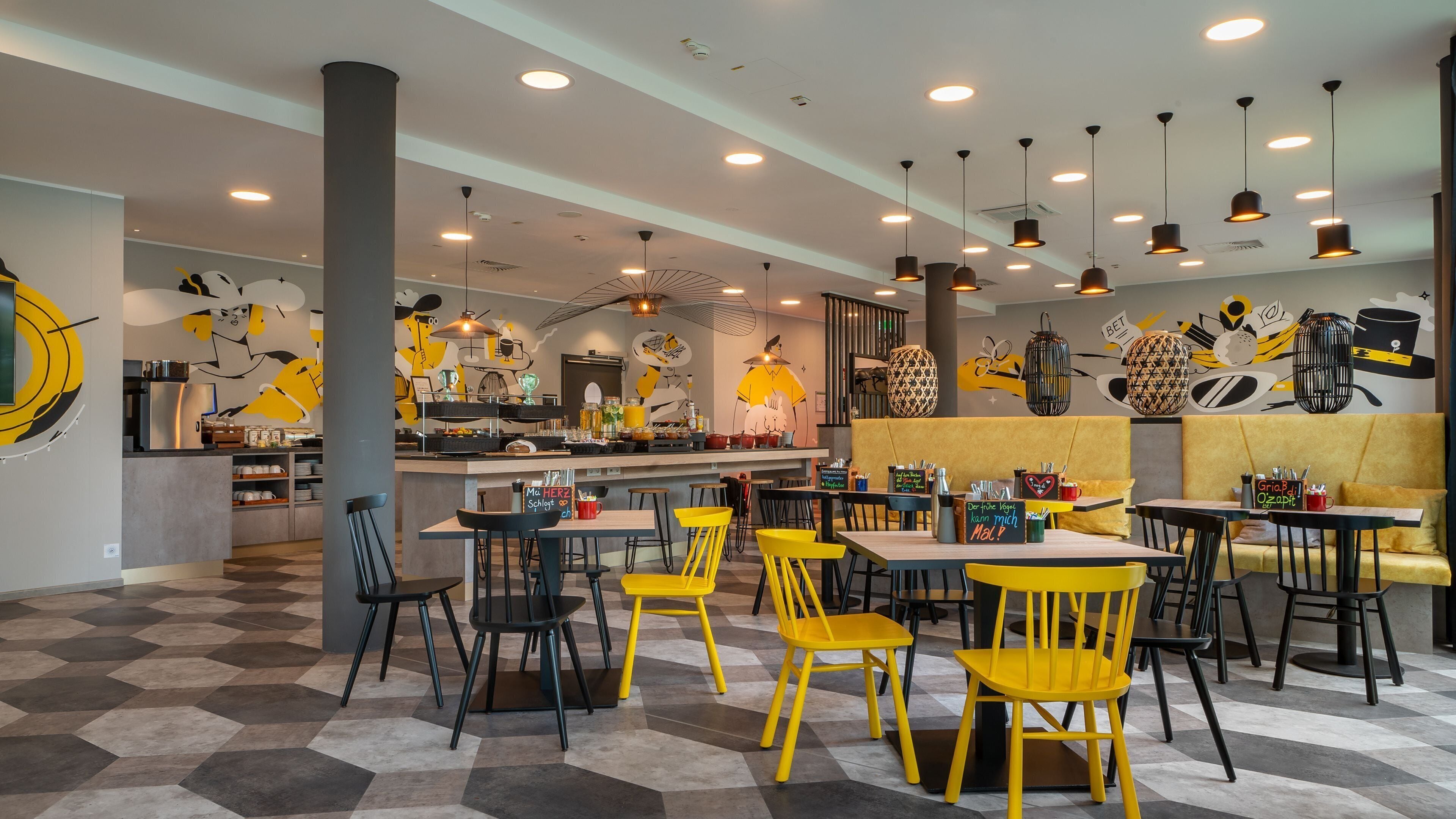 A restaurant interior with hexagonal patterned flooring, yellow and black chairs, and a central bar area.
