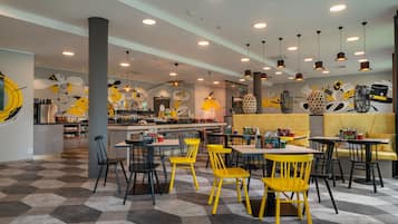 A restaurant interior with hexagonal patterned flooring, yellow and black chairs, and a central bar area.