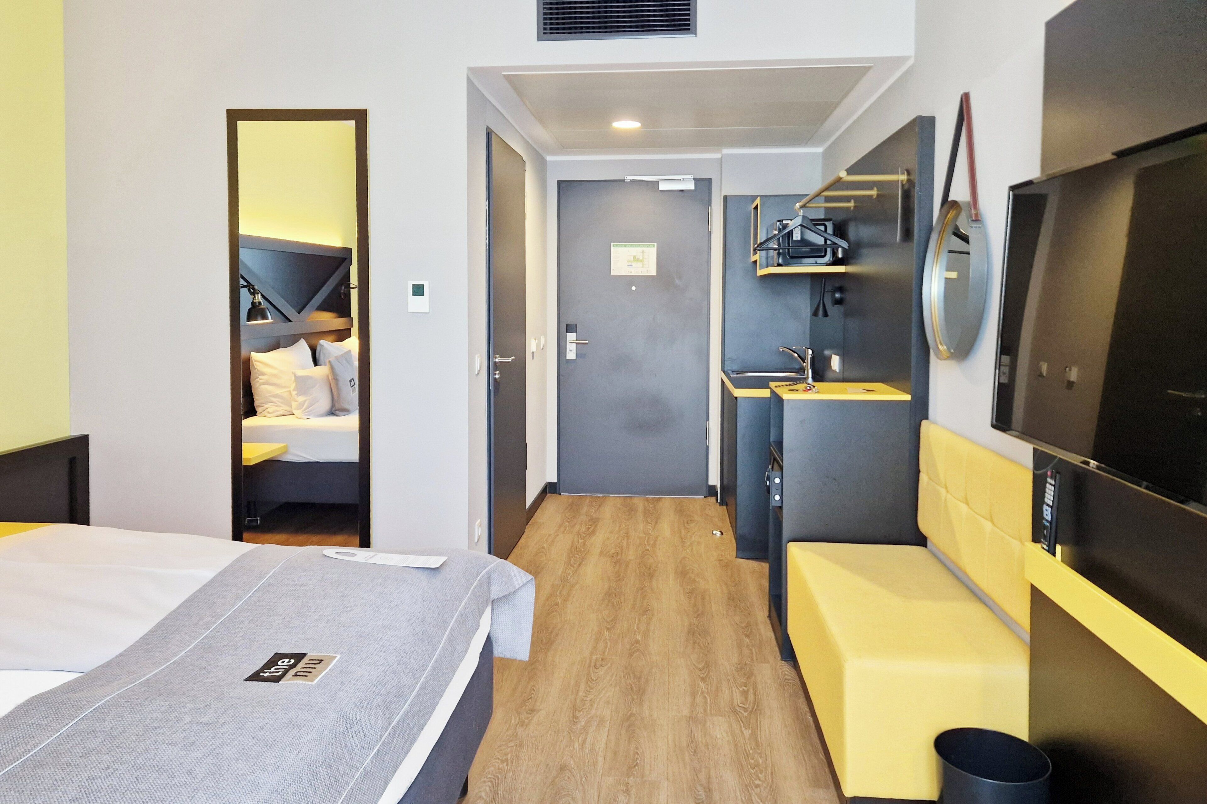 A hotel room with a bed, a small kitchenette, a mirror, and a television.