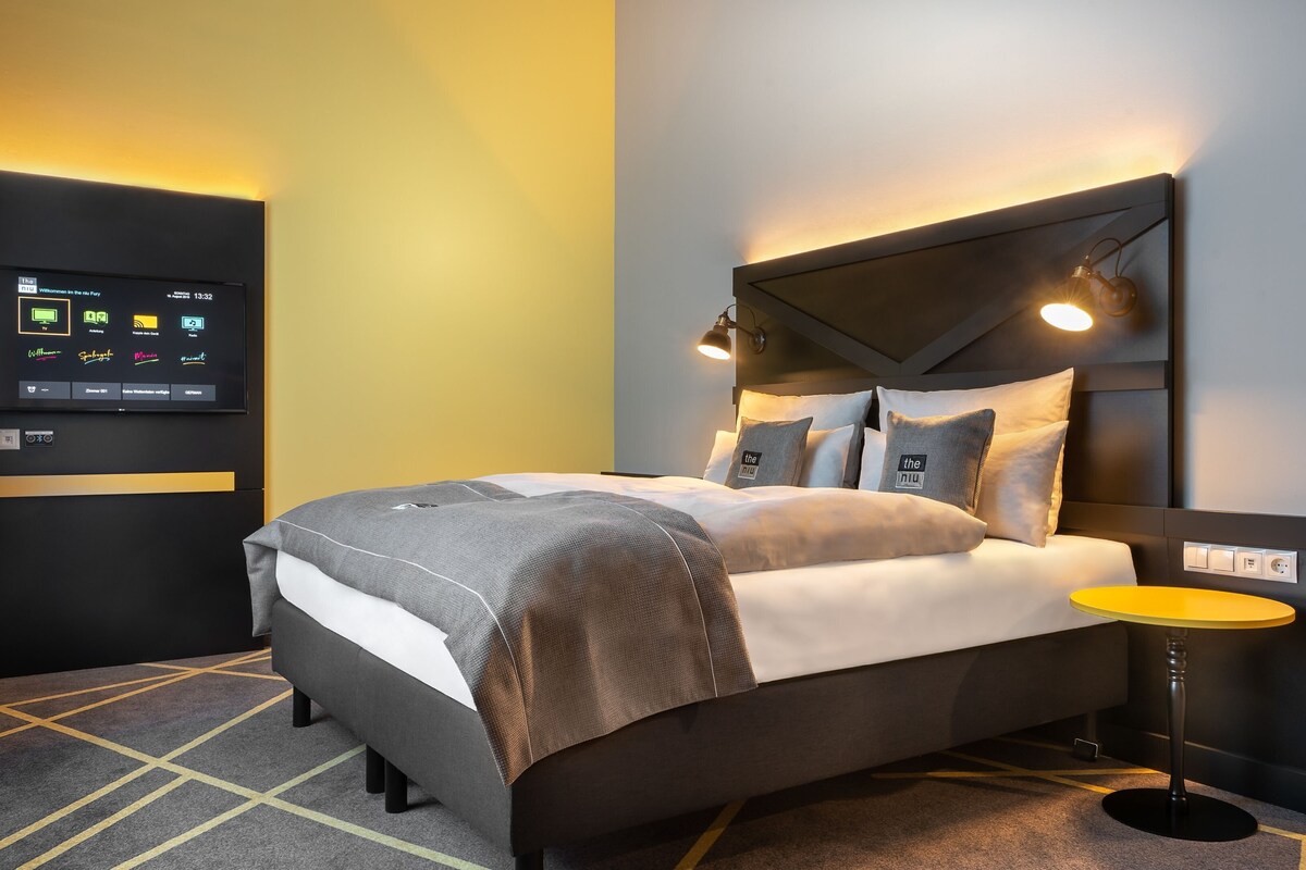 Une chambre d’hôtel moderne équipée d’un lit, d’une table de chevet et d’un panneau de commande numérique fixé au mur.