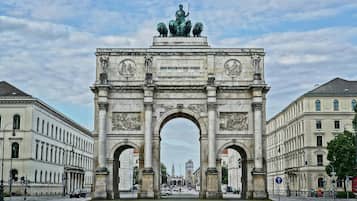 Un gran arco de piedra con inscripciones y estatuas, flanqueado por edificios de estilo clásico.