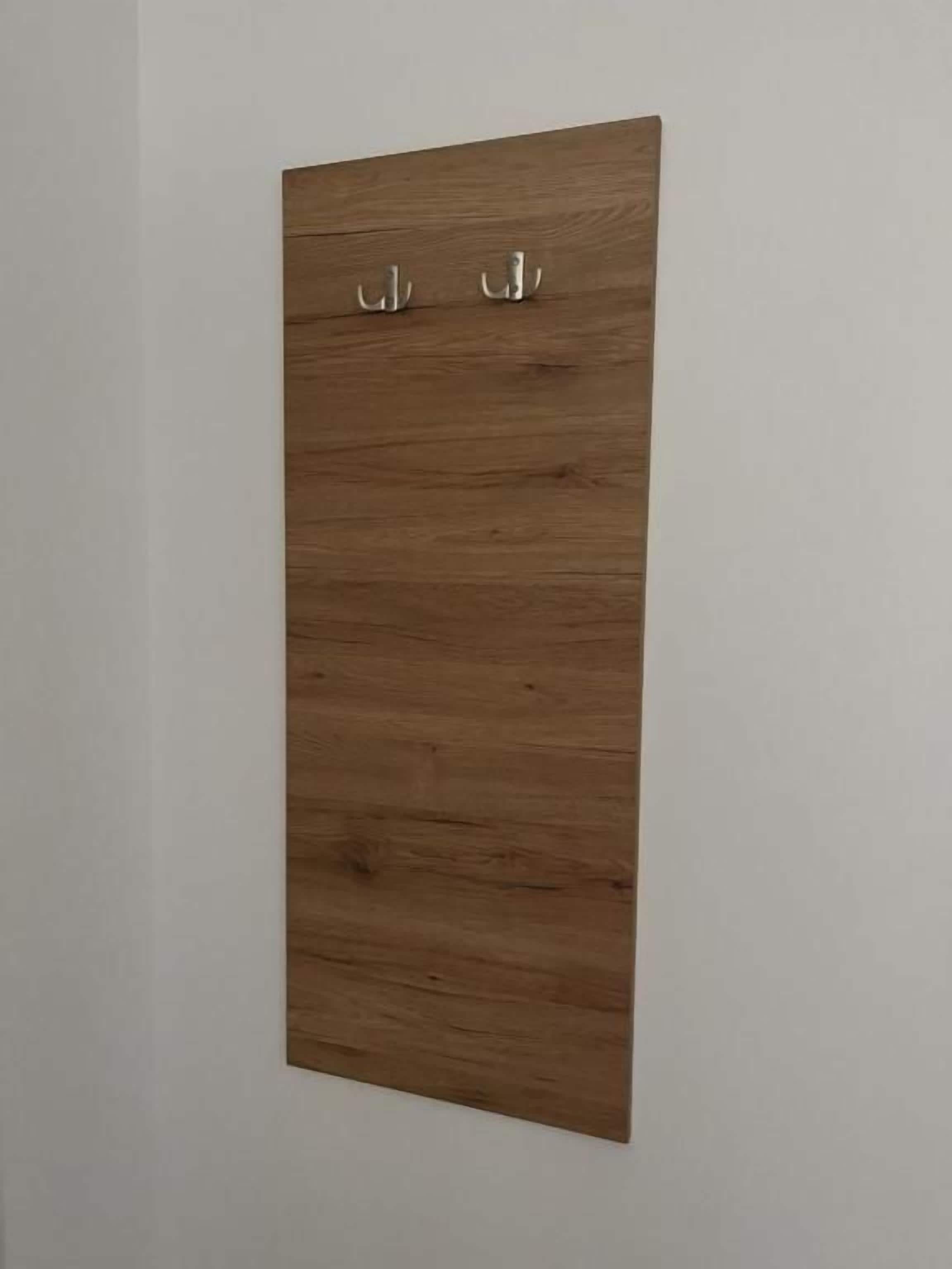Eine Holzplatte mit zwei Haken an einer weißen Wand.