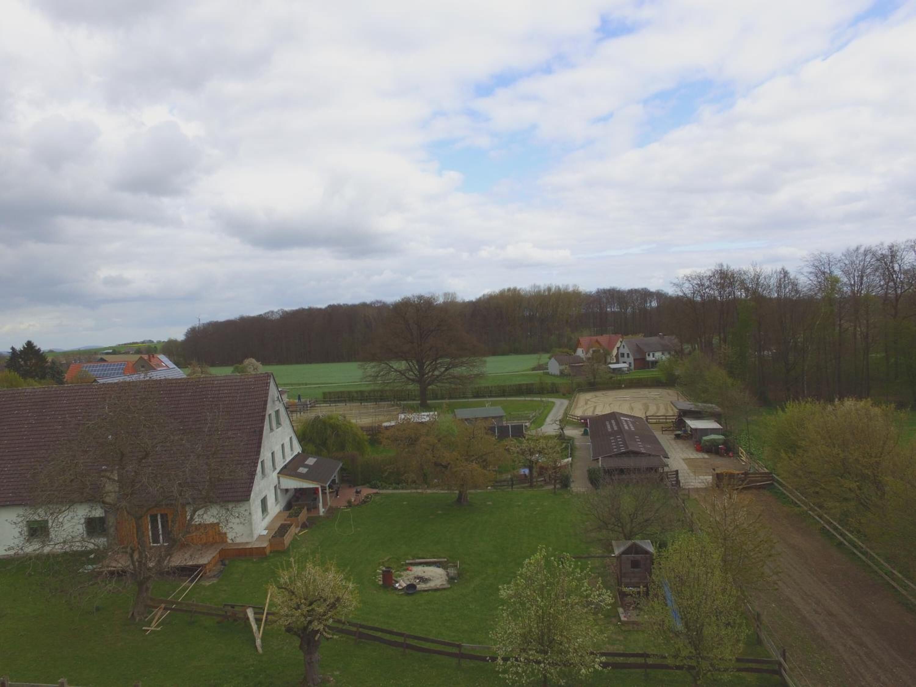 A rural landscape with a large white house, a fenced yard, and a small wooden structure.