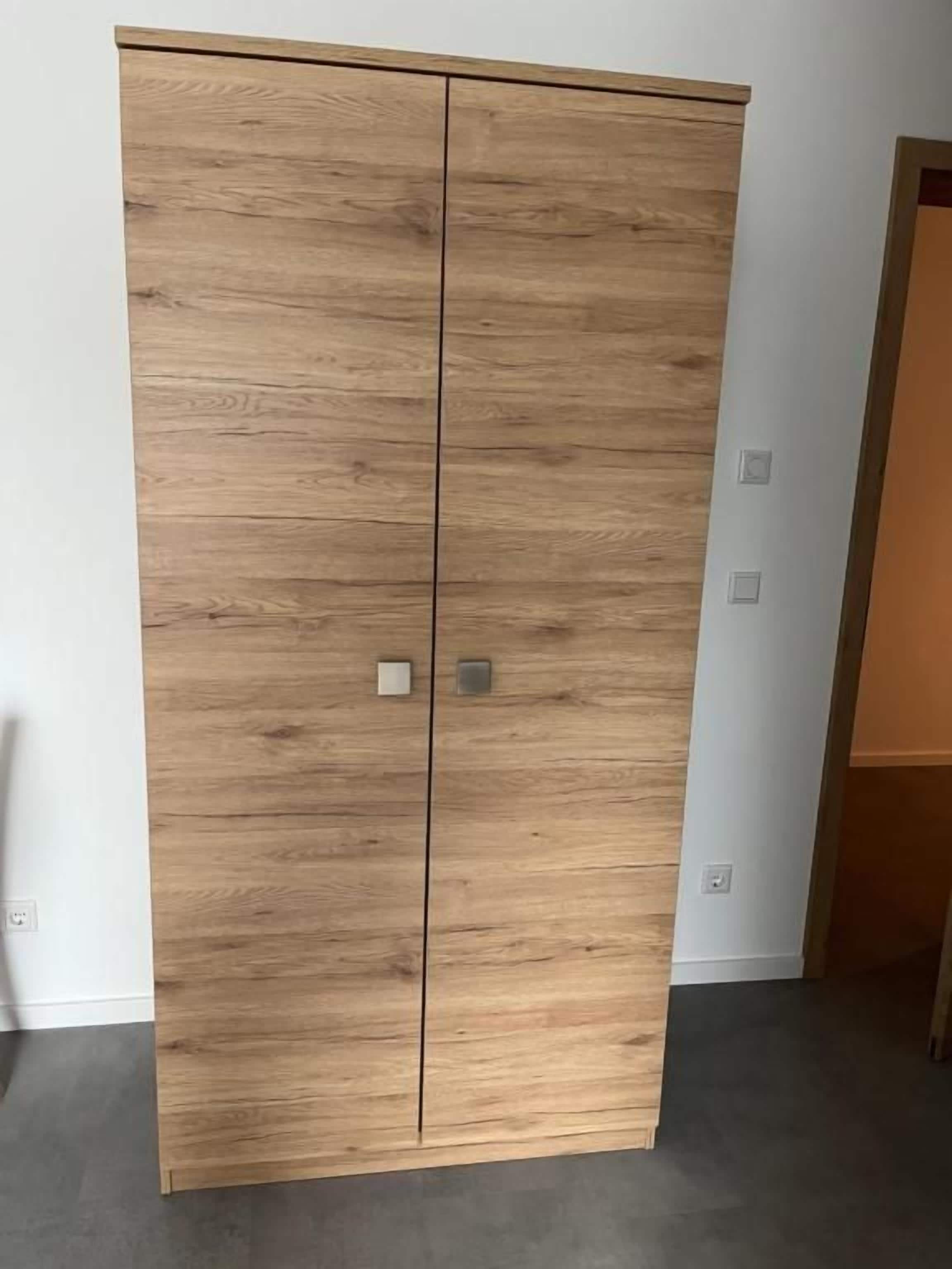 Ein Holzkleiderschrank mit zwei Türen und einem Griff.