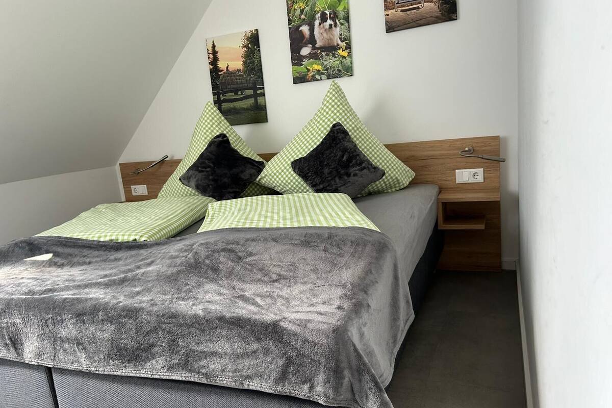 A bedroom with a bed, green and black pillows, a grey blanket, wooden headboard, and two nightstands.
