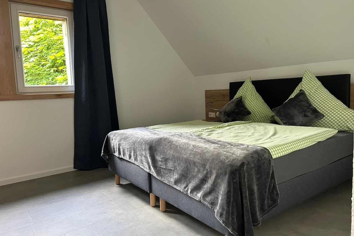 A bedroom with a bed, a window with curtains, and a view of greenery outside.